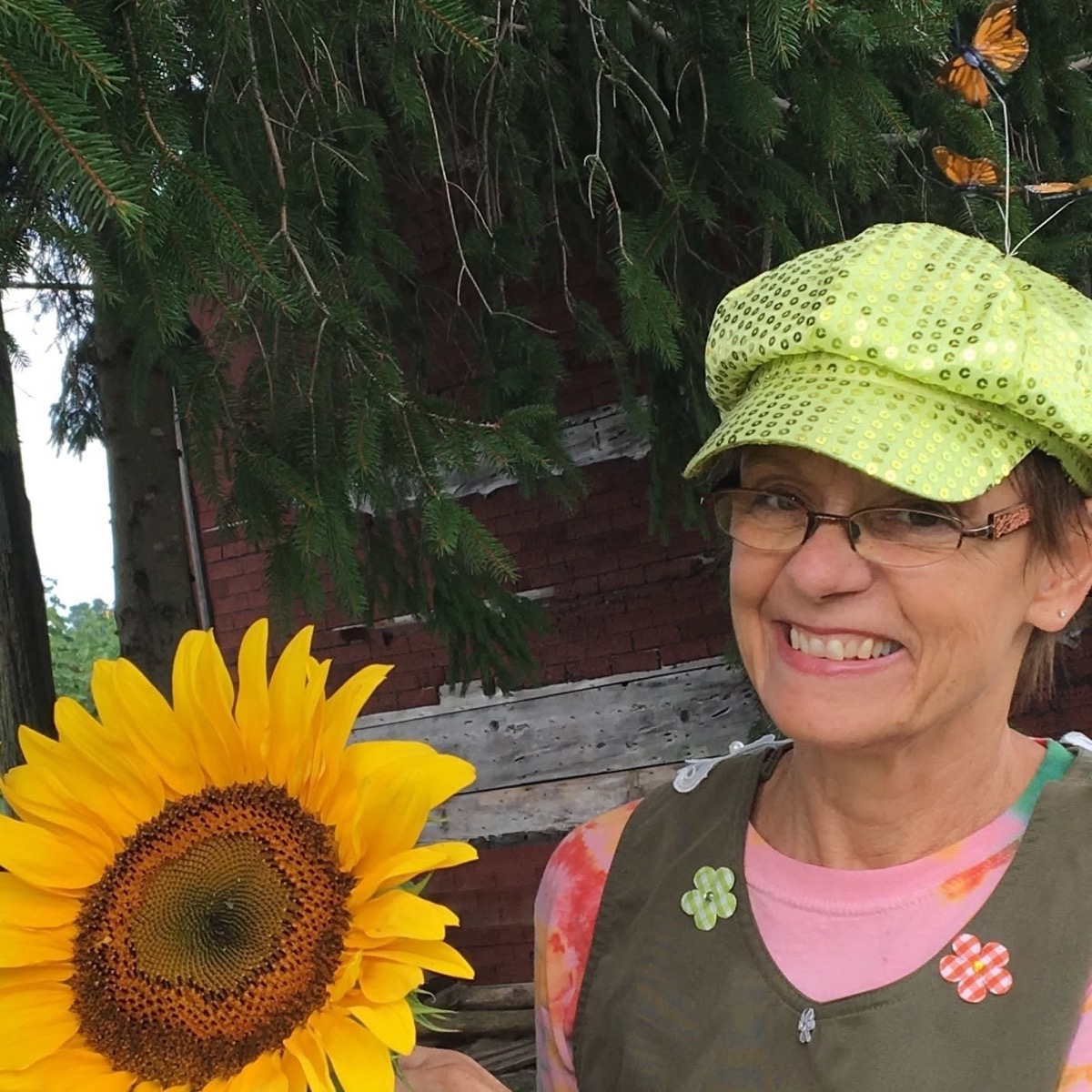Elaine Cooper, Grandma Greenthumb, smiling in her green hat holding a large sunflower